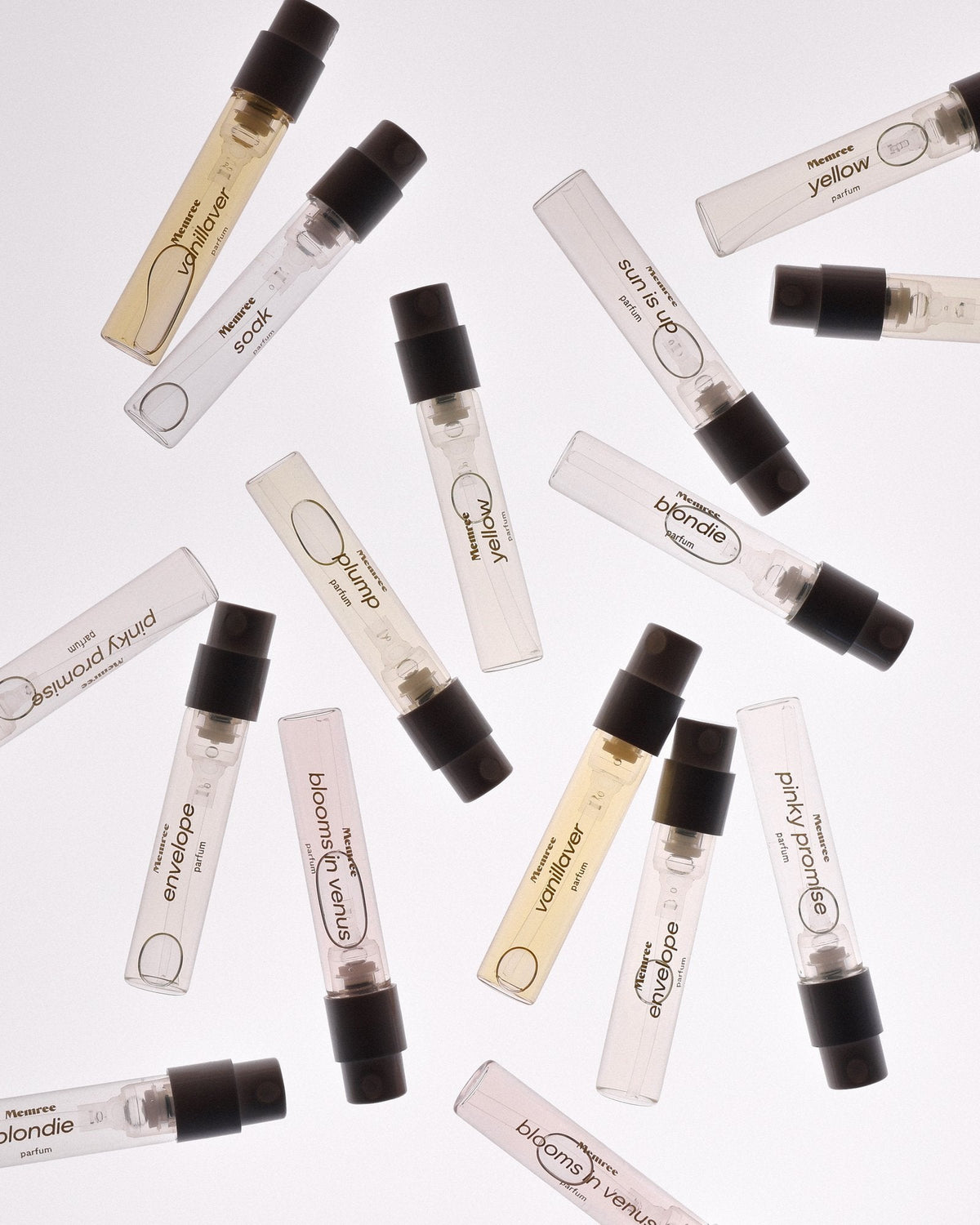 Glass sample vials of perfume scattered across a pale surface