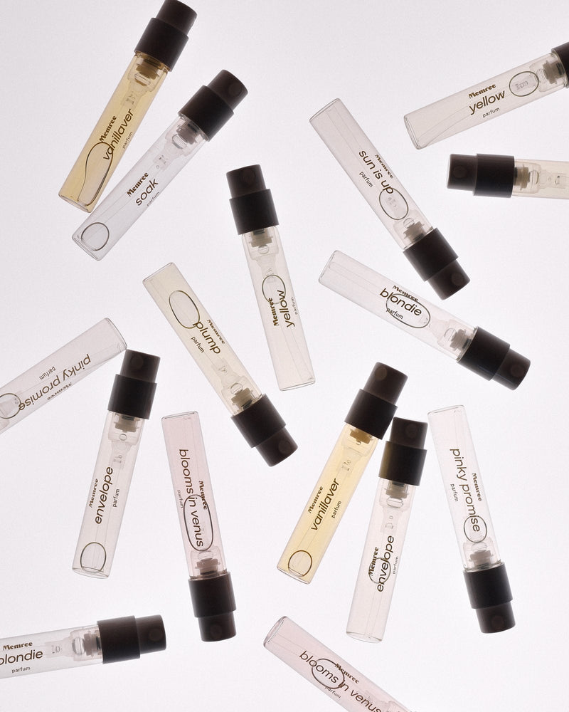 Glass sample vials of perfume scattered across a pale surface