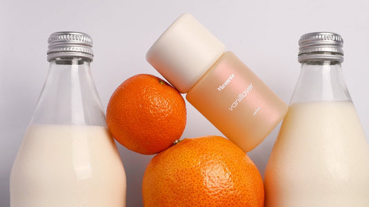 A parfum bottle resting on a fridge shelf between milk bottles and oranges